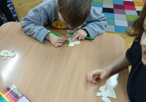 Chłopiec siedzi przy stoliku i markerami dekoruje drewnianą dekoracje świąteczną wg. własnego pomysłu.