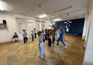 Dzieci ustawione w rozsypce powtarzają ruchy taneczne za prowadzącą warsztaty z zumby.