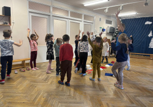 Dzieci stoją z rękami uniesionymi do góry podczas rozkładania ścieżki sensorycznej.