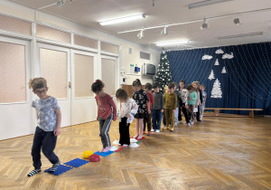 Dzieci ustawione w pociąg przechodzą przez ścieżkę sensoryczną z bosymi stopami.