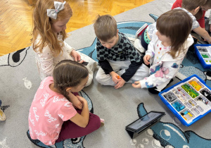 Trzy dziewczynki i chłopiec budują konstrukcję z klocków wg instrukcji wyświetlanej na tablecie.