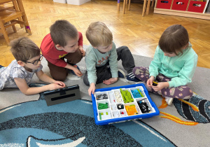 Dziewczynka i trzech chłopców buduje konstrukcję z klocków wg instrukcji wyświetlanej na tablecie.