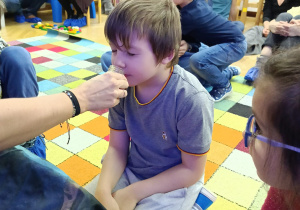 Chłopiec z zamkniętymi oczami stara się rozpoznać zapach znajdujący się w słoiczku.