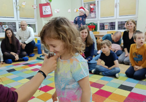 Dziewczynka z zamkniętymi oczami stara się rozpoznać zapach znajdujący się w słoiczku.
