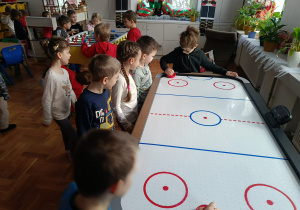 Dzieci stoją przy stolikach i testują znajdujące się na nich gry na świetlicy szkolnej.