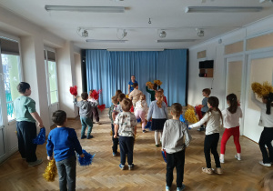 Dzieci stoją w rozsypce z kolorowymi pomponami w rękach i uczą się nowej choreografii tanecznej na zajęciach z zumby.