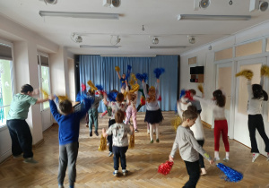 Dzieci stoją w rozsypce z rączkami splecionymi przed sobą i uczą się nowej choreografii tanecznej na zajęciach z zumby.