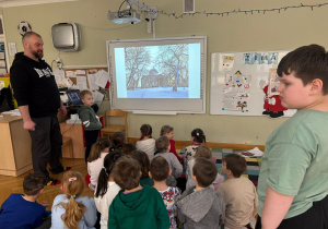 Dzieci siedzą na dywanie i oglądają prezentację przedstawiającą pracę w Muzeum Królikarni przygotowaną przez tatę kolegi w ramach projektu Bohater Tygodnia.