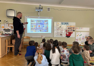 Dzieci siedzą na dywanie i oglądają prezentację przedstawiającą pracę w Muzeum Królikarni przygotowaną przez tatę kolegi w ramach projektu Bohater Tygodnia.