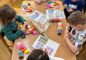 Trzy dziewczynki i dwóch chłopców siedzi przy stoliku i lepią wybrane przez siebie kształty z piankoliny przyniesionej przez kolegę w ramach projektu Bohater Tygodnia.