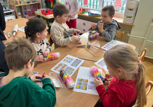 Dwie dziewczynki i trzech chłopców siedzi przy stoliku i lepią wybrane przez siebie kształty z piankoliny przyniesionej przez kolegę w ramach projektu Bohater Tygodnia.