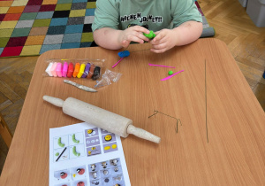 Chłopiec siedzi przy stoliku i lepi wybrane przez siebie kształty z piankoliny przyniesionej przez kolegę w ramach projektu Bohater Tygodnia.