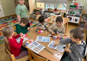 Dwie dziewczynki i trzech chłopców siedzi przy stoliku i lepią wybrane przez siebie kształty z piankoliny przyniesionej przez kolegę w ramach projektu Bohater Tygodnia.