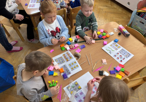 Dwie dziewczynki i dwóch chłopców siedzi przy stoliku i lepią wybrane przez siebie kształty z piankoliny przyniesionej przez kolegę w ramach projektu Bohater Tygodnia.