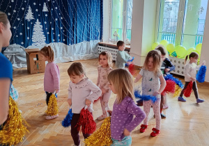 Przedszkolaki stoją w rozsypce i trzymają pompony na wysokości bioder.