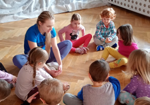 Przedszkolaki siedzą na podłodze i wykonują ćwiczenie rozluźniające - motylka.