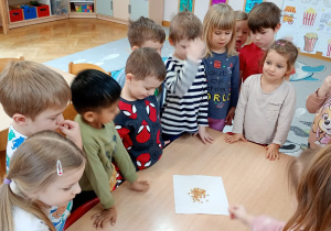 Dzieci stoją wokół stolika, na którym rozłożone są ziarna kukurydzy.