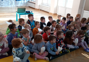 Dzieci siedzą na materacach i podczas oglądania filmu zjadają popcorn ze swoich rożków.