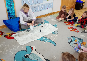 Przedszkolaki obserwują przeprowadzany przez prowadzącą eksperyment.