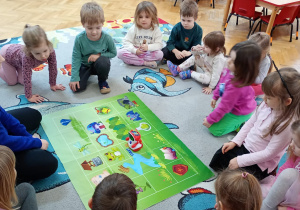 Dzieci siedzą wokół zielonej maty i obserwują przesuwanie się po niej robota.