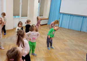 Dzieci stoją z rękami na biodrach i wykonują krążenia głowy.