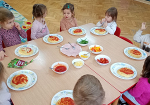 Maluchy nałożyły na swoje pizze sos pomidorowy i czekają na posypanie ich serem.