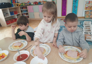 Dziewczynka nakłada na swoją pizzę pomidorki koktajlowe.