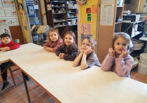 Trzy dziewczynki i dwóch chłopców siedzą przy wysokim i długim stole w Pracowni Ceramicznej "Amfora".