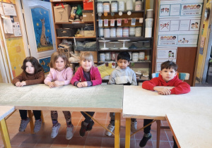 Trzy dziewczynki i dwóch chłopców siedzą przy wysokim i długim stole w Pracowni Ceramicznej "Amfora".