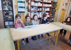 Cztery dziewczynki i chłopiec siedzą przy wysokim i długim stole w Pracowni Ceramicznej "Amfora".