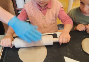 Dziewczynka wałkuje kawałek gliny na cienki placuszek.