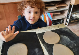 Chłopiec rozklepuje otwartą dłonią kawałek gliny znajdujący się na ceracie.