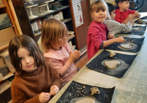 Trzy dziewczynki i dwóch chłopców formują małe kuleczki z nadmiaru gliny.