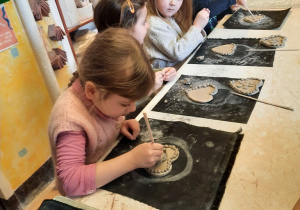 Dziewczynka za pomocą patyczka ozdabia wnętrze kwiatuszka, ulepionego i przyklejonego na środku serca.