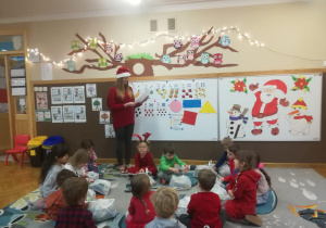 Dzieci siedzą na dywanie, a nauczycielka czyta list od Świętego Mikołaja.