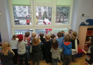 Dzieci stoją przy parapecie machając Świętemu Mikołajowi na powitanie.