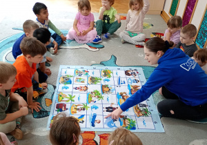 Prowadząca wskazuje przedszkolakom na macie pole, na które ma dotrzeć robot.