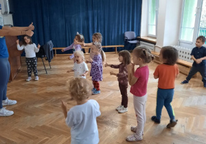Dzieci stoją z wyciągniętymi rękoma do przodu i pokazują kciuk podniesiony w górę.