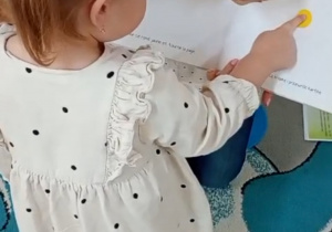 Dziewczynka naciska na żółtą kropkę w książce.