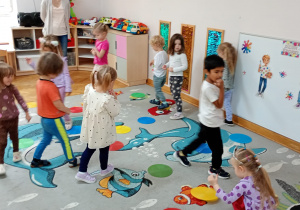 Przedszkolaki chodzą w rytm muzyki pomiędzy rozłożonymi na dywanie krążkami.