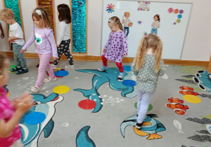 Przedszkolaki chodzą w rytm muzyki pomiędzy rozłożonymi na dywanie krążkami.