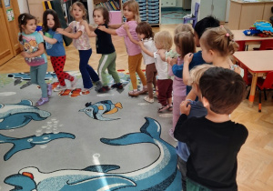 Dzieci trzymając się za ramiona tworzą węża, który porusza się po dywanie.