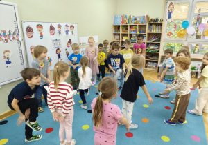 Dzieci chodzą po dywanie, podnoszą jedną nogę i klaszczą pod kolanem.