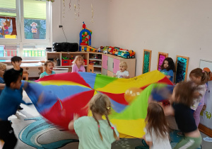 Maluchy poruszają chustą animacyjną podrzucając na niej balonik.