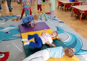Dwie dziewczynki i chłopiec turlają się po rozłożonych na dywanie materacach.