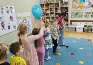 Starszaki stoją jeden za drugim i podają sobie balon nad głową.