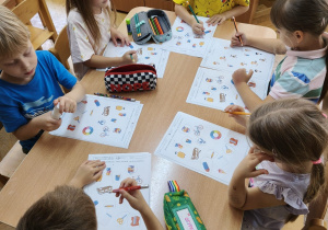 Dzieci siedzą przy stoliku i wykonują kartę pracy związaną z Dniem Przedszkolaka.