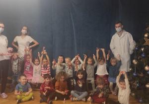 Dzieci siedzą na dywanie trzymając w rękach szczoteczki i pasty do zębów otrzymane od studentów stomatologii.