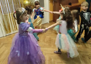 Dziewczynki tańczą trzymając się za ręce podczas balu karnawałowego.