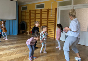 Dzieci wykonują krok taneczny za instruktorką zumby.